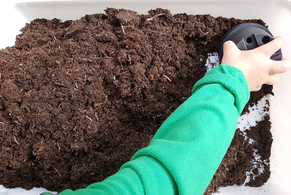 A childs arm and hand playing with compost in a tub