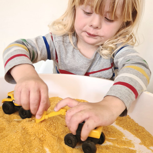 boy in grey tshirt playing with mini digger toys in cereal sand