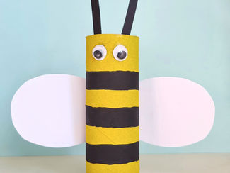 Bee made from a toilet roll inner, with googly eyes and paper wings, on a pale blue background