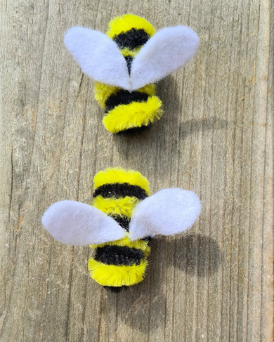 Two bees made from pipecleaners and felt sitting on a wooden table