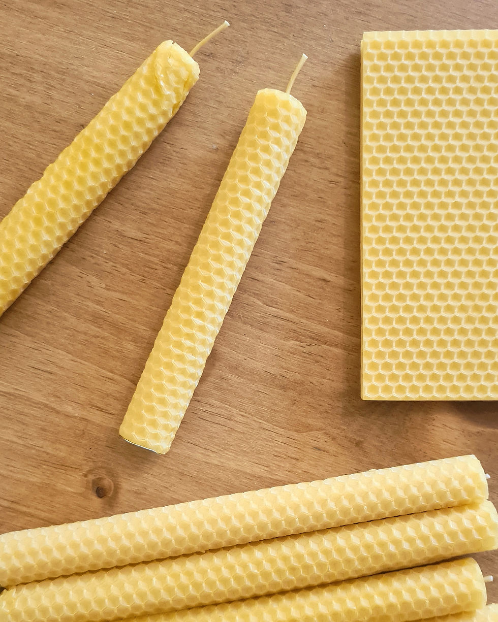 Yellow beeswax candles and a honeycomb sheet on a wooden surface.