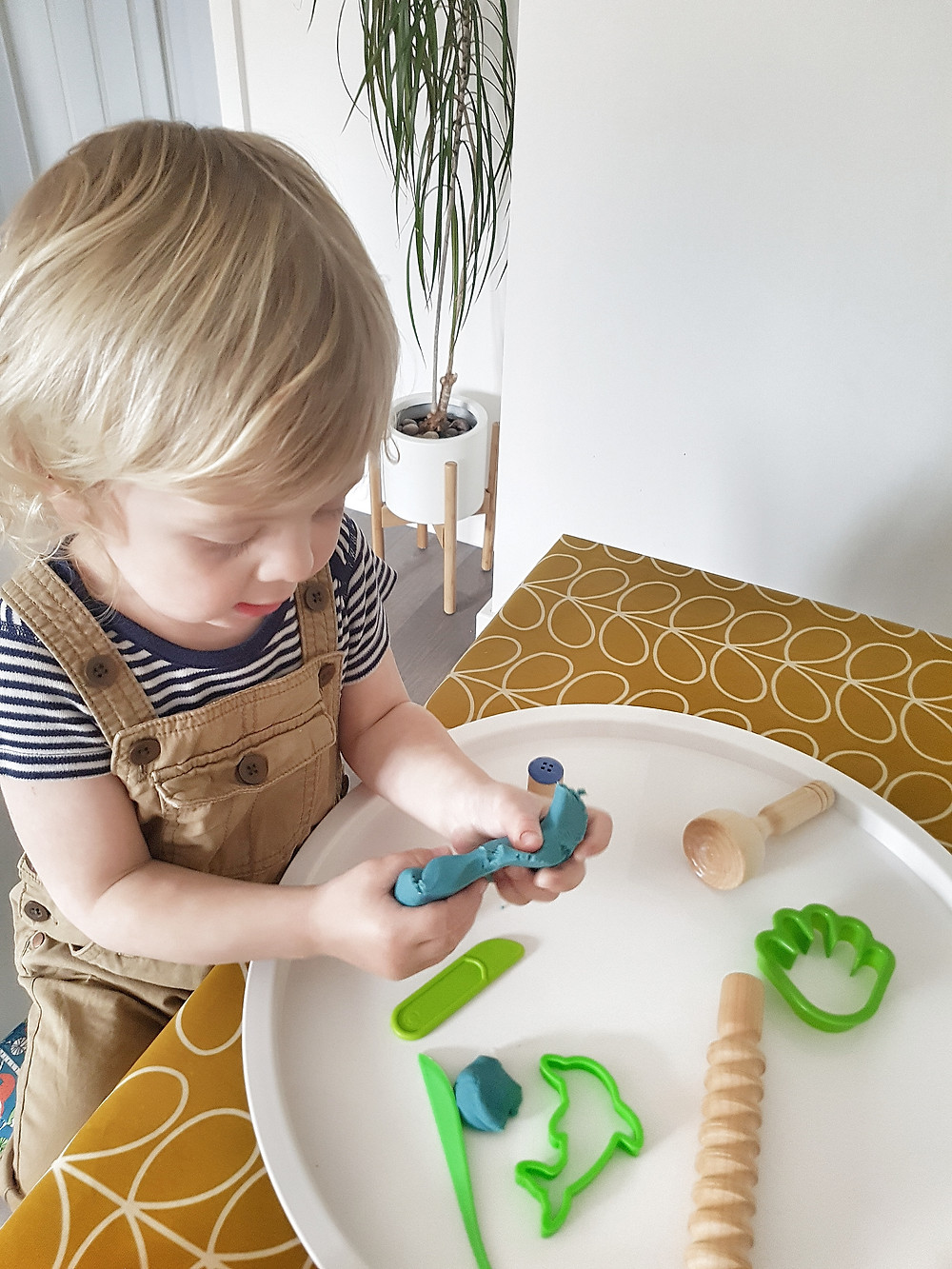 blond toddler playing with blue playdough at table