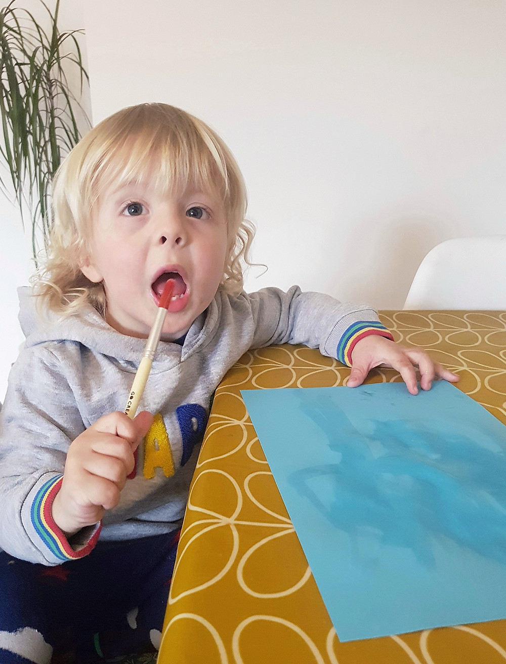 blonde toddler trying to eat paintbrush