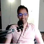 headshot of a smiling south Asian man with glasses and a pink shirt