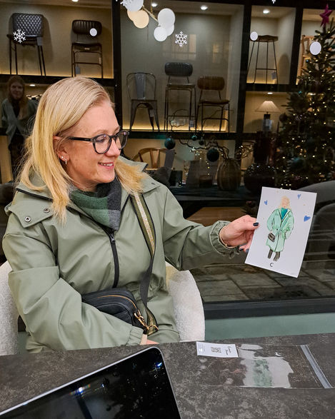 a woman holds up a drawing of a woman in a green coat