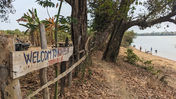 A hand-painted sign welcoming hikers to the national forest. The sign is on a wooden board nailed to a fence under a tree next to a river.