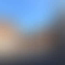 The industrial-style courtyard of the Risiera di San Sabba. The red brick buildings stand empty, towering over the enclosed space. A black spire rises out of the ground, symbolising a crematorium's smokestack. A woman stands beneath the smokestack, contemplating its significance.