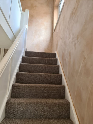 Carpeted staircase with white railing leading upward along neutral toned wall