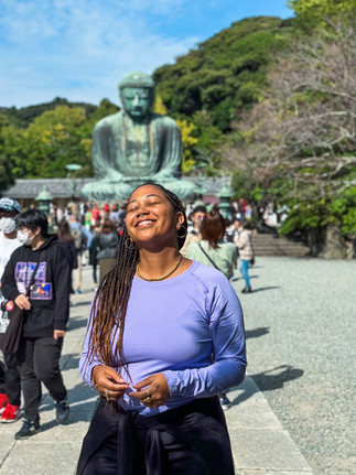 Anela in Japan standing in front of the buddha statue in Kamakura, smiling with her face turned up to the sun