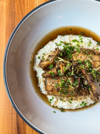 an up close image of big bowl on a wooden table at The Garage, a Black-owned restaurant in Savannah, GA. Inside the bowl lies crispy catfish, with rice grits underneath, and brown butter and seared mushrooms.
