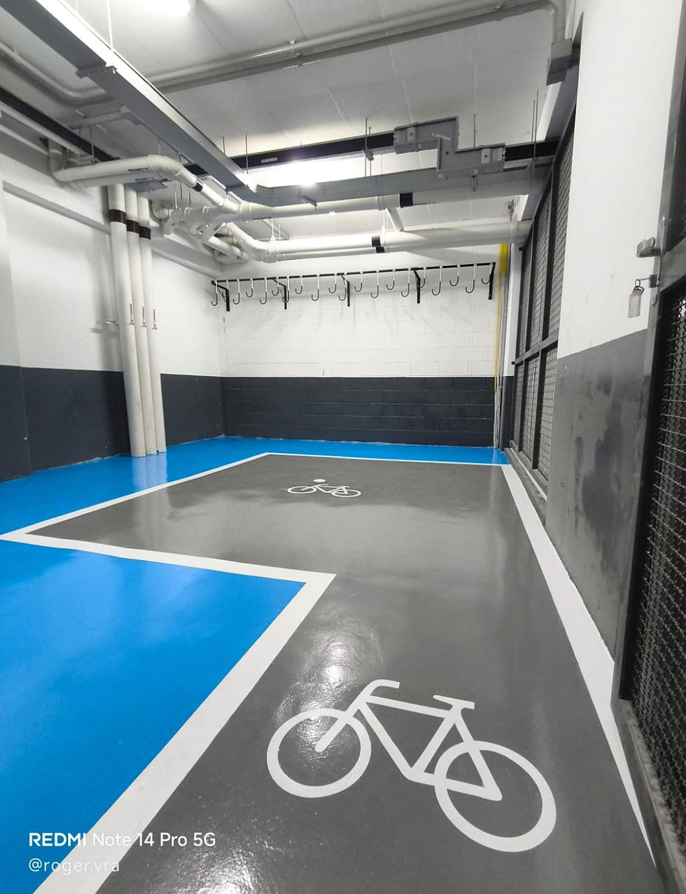 Estacionamento coberto para bicicletas com piso azul e cinza.