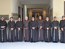 Grupo de nueve frailes franciscanos en un pasillo