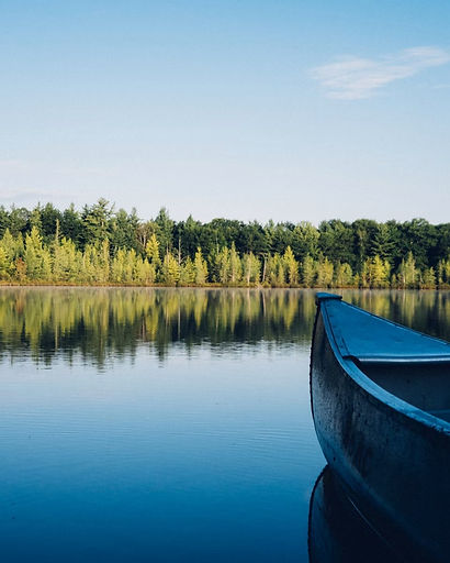 A canoe on calm water in front of tall trees at a summer camp
