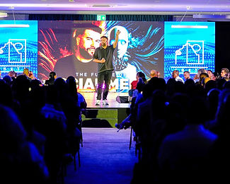 A speaker presenting on stage to a packed conference audience