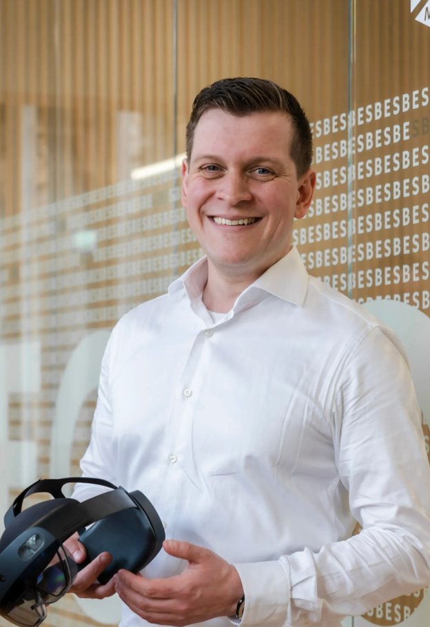 Portrait of Jonas Heller smiling in a white shirt, holding a mixed reality headset
