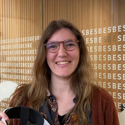 Portrait of Mariska Geerts smiling, wearing glasses and holding a VR headset