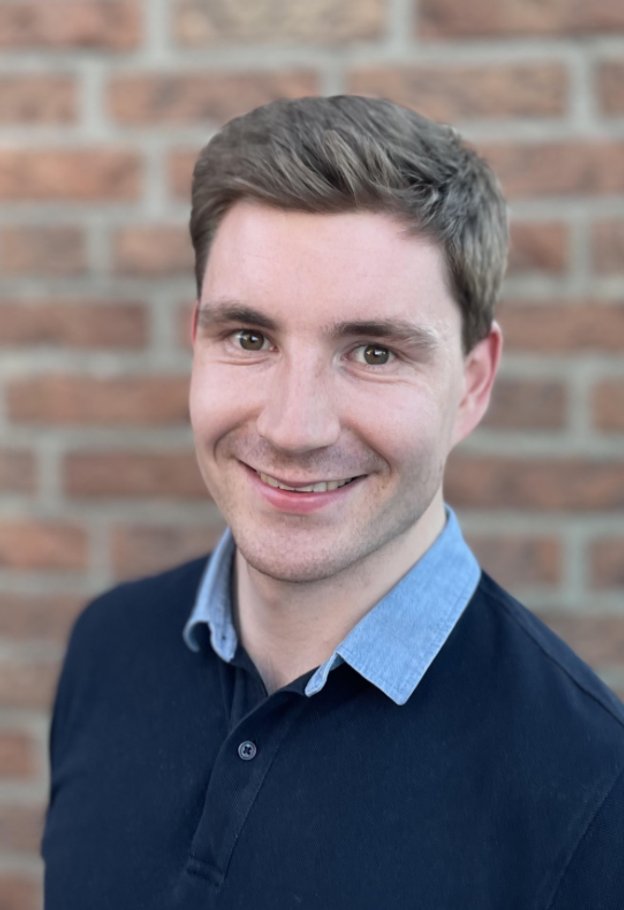 Portrait of Marc Becker smiling in front of a brick wall