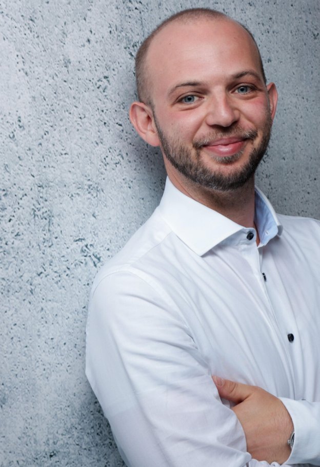 Portrait of Roman Briker leaning against a concrete wall in a white shirt