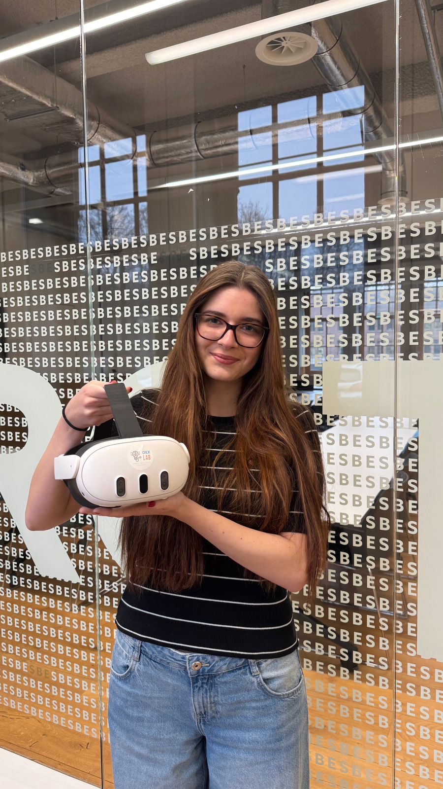 Paula Wodecka standing in a glass-walled hallway, holding a VR headset
