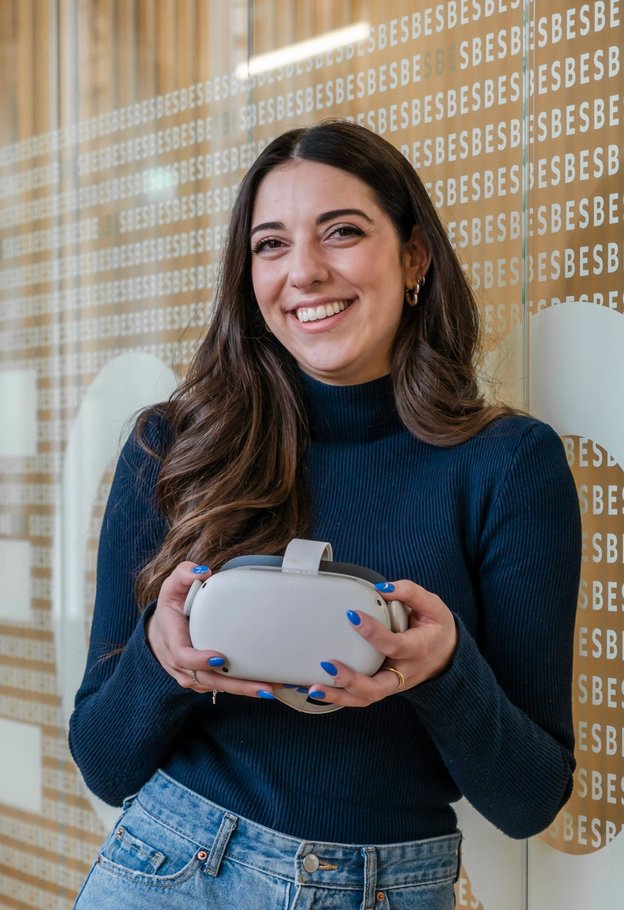 Portrait of Roberta Di Palma smiling in a navy sweater, holding a VR headset