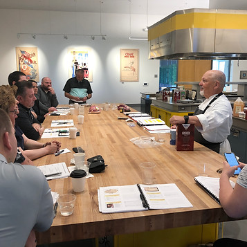Members of the Tyson Fresh Meats Foodservice team sitting around a table listening to Master Chef Tony Seta talking