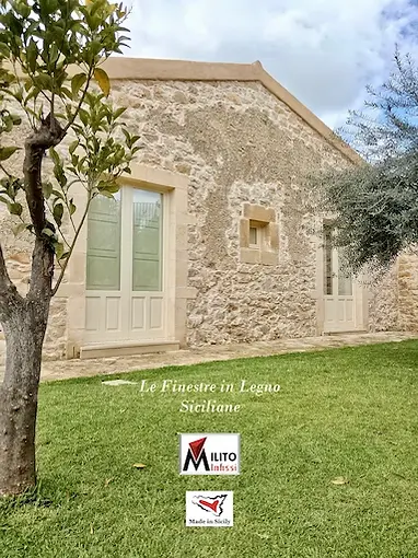 Elegant white wooden french doors integrated into the traditional stone facade of a luxury Sicilian masseria.