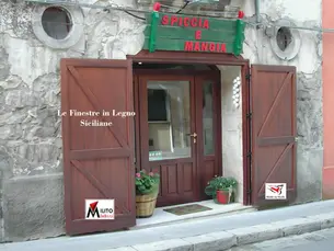Portelloni esterni in legno massiccio a doghe e infisso d'ingresso integrati in una facciata in pietra nel centro storico di Scicli.