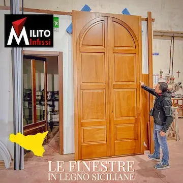 Le proporzioni imponenti di un portone ad arco in legno per centri storici, mostrate da un artigiano di Milito Infissi in laboratorio.