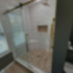Custom walk-in shower with marble-look tile, pebble mosaic floor, built-in bench, niche and brass fixtures.