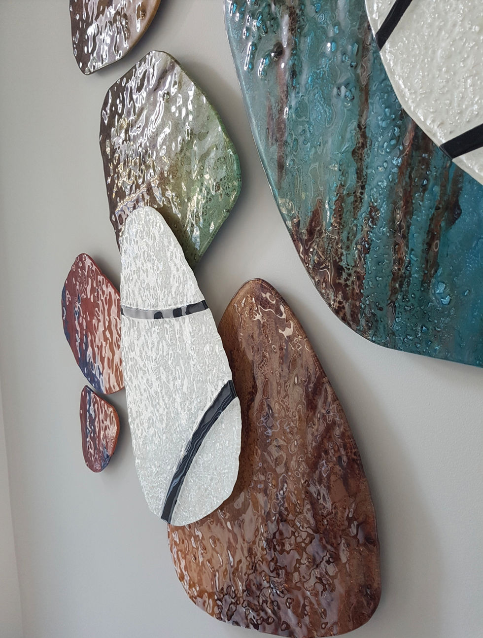 This beautiful glass art installation works with texture, soft shapes and a full spectrum of colours in earthtones that move into jewel tones. the second layer is white with black lines that create a circle geometric design over the sculpture.