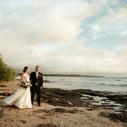 Bride and groom walking together on a wide rocky beach during a beautiful dramatic sunset in Costa Rica