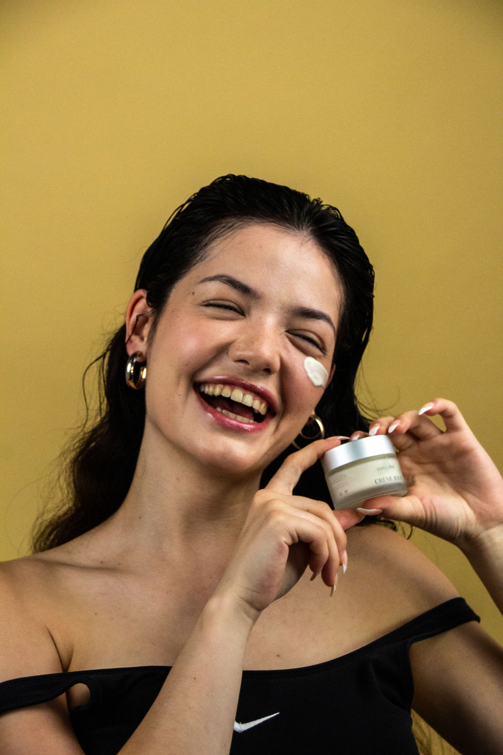 Shooting beauté campagne cosmétique, modèle naturel au sourire lumineux tenant un soin visage, direction artistique moderne