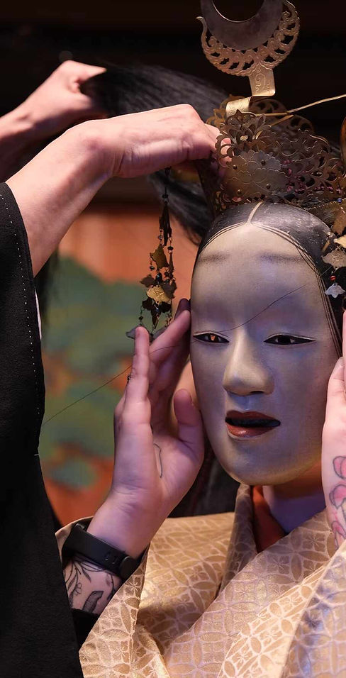 des mains qui placent un masque de thêatre japonais sur le visage d'une femme