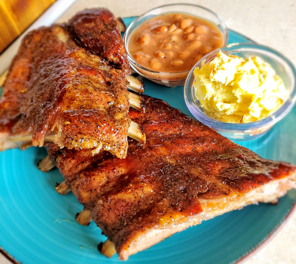 Barbecue ribs on a bbq plate with sides of beans and potato salad in clear bowls. The setting is bright and appetizing.