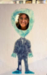 Ana puts her head into a painting of a green alien that wears a black suit.