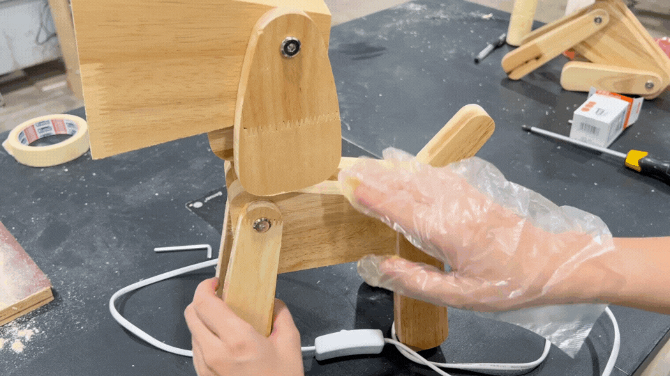 Applying wood wax to a wooden lamp piece with gloves on, ensuring a protective finish.