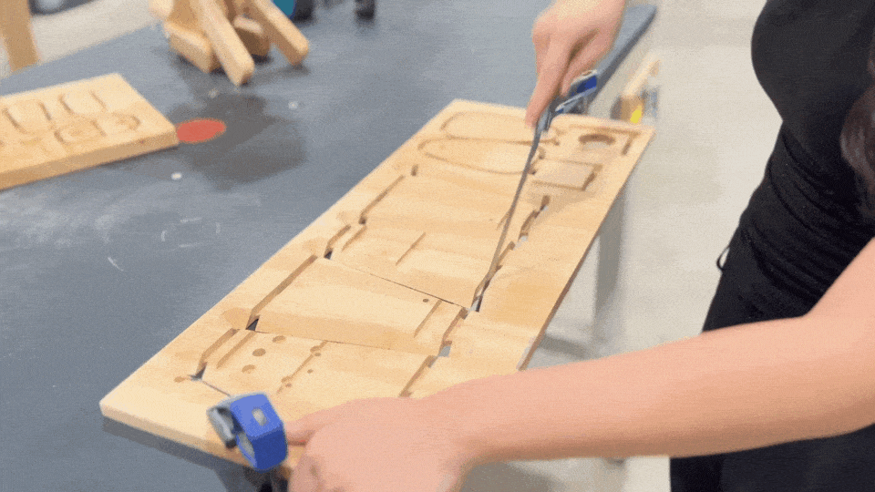 Person using a hand saw to cut a wooden board for crafting a lamp during the initial preparation phase.
