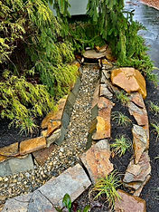 Stone-lined drainage channel with gravel and planting.
