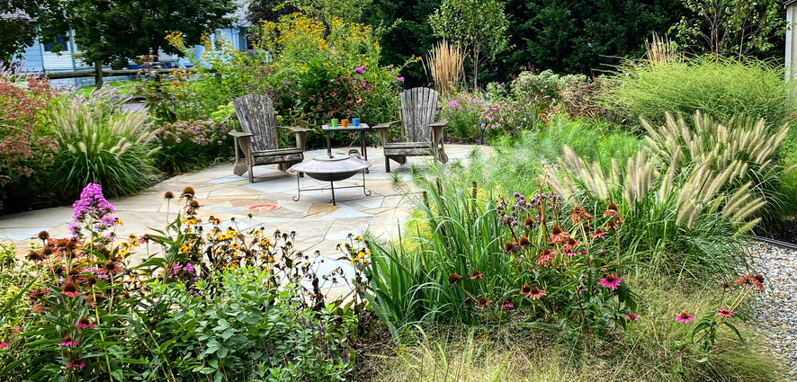 Stone patio with Adirondack chairs surrounded by grasses and layered planting. 