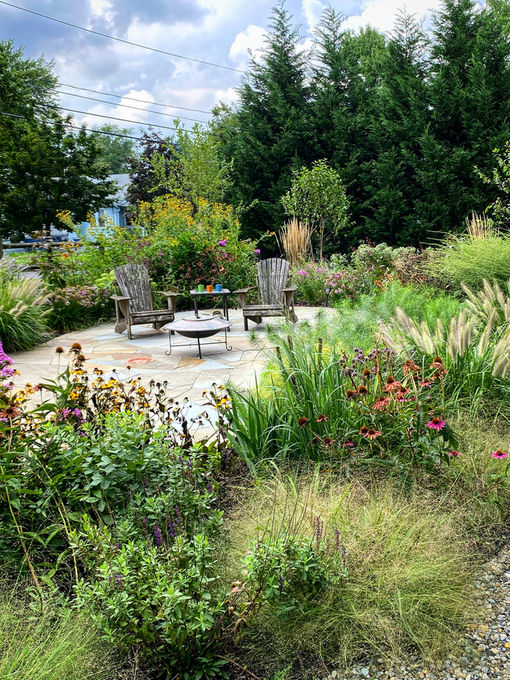 Stone patio with Adirondack chairs surrounded by grasses and perennials in a plant-forward garden.