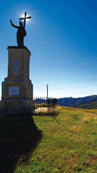 Statua con croce su piedistallo in cima a una collina erbosa