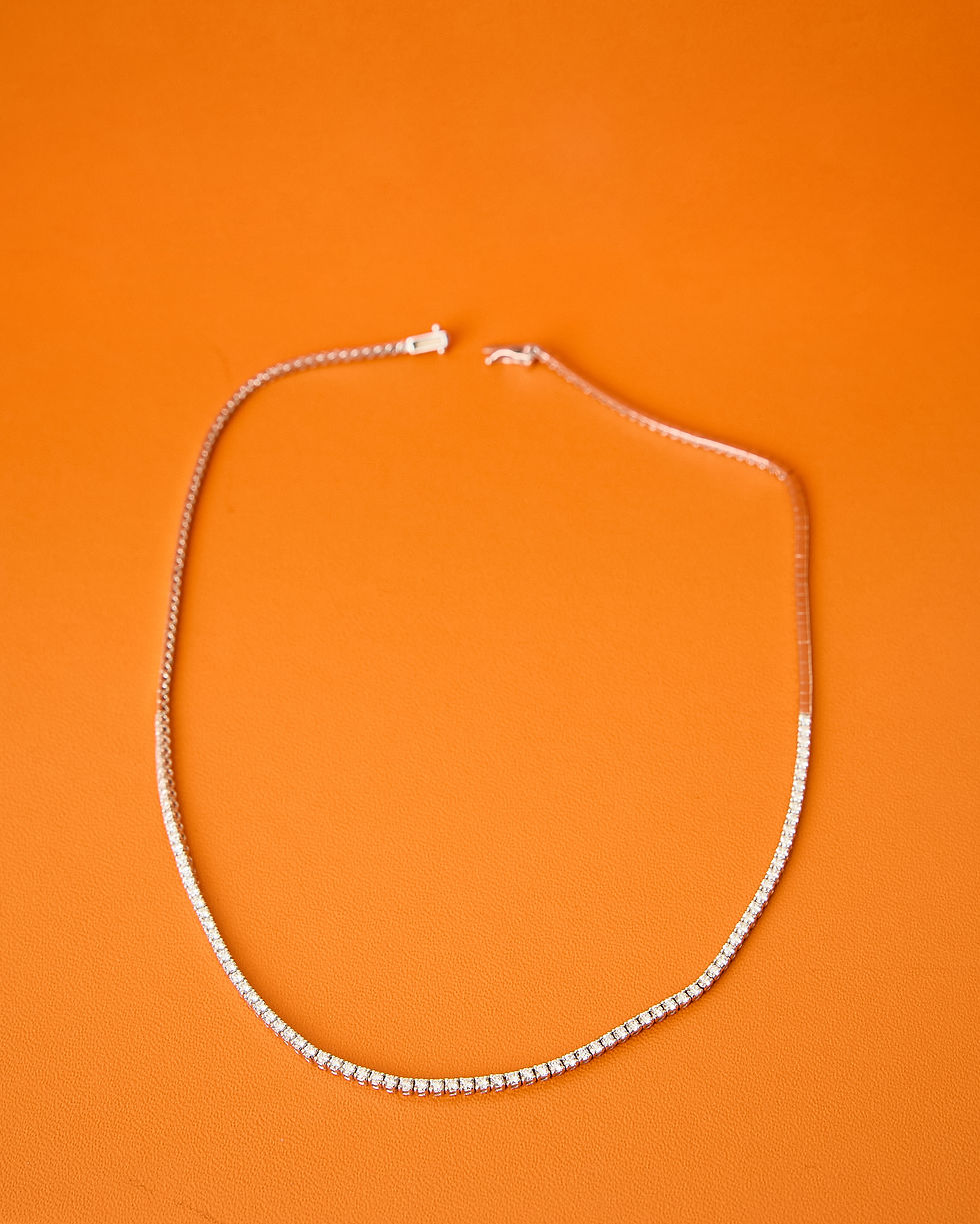 The Diamond Riviera Tennis Necklace showcased on a beautiful orange background