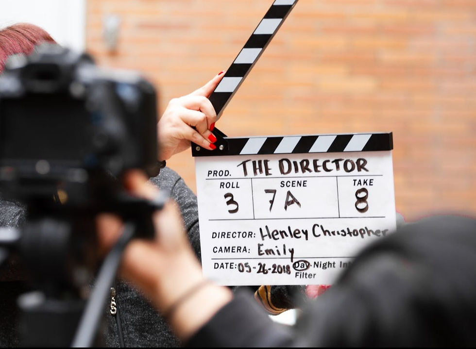 A film clapboard reads "The Director," Roll 3, Scene 7A, Take 8. Hands hold it on set, camera and brick wall in background. Date: 05-26-2018.