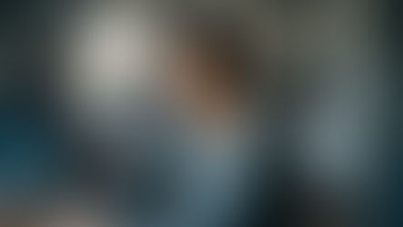 Pessoa sentada à mesa com outras pessoas ao fundo em leve desfoque, com expressão pensativa e contida, transmitindo o medo de decepcionar ao começar a mudar.