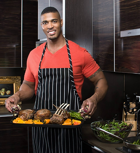 Chef Shawn Osbey wearing a black and white striped apron over a red t-shirt, presenting a tray of gourmet steak, lamb chops,