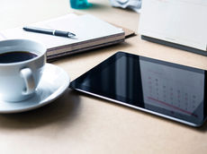 a coffee, ipad, and notepad on a desk 