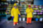 A color photo of two workers in colorful raincoats outside a New York bodega, 2010. New York wall art print for sale.