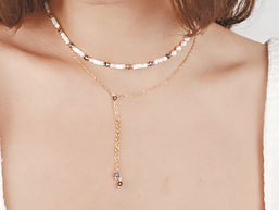 Frau trägt eine goldene Y-Kette mit weißen Muschelperlen und blauen Kristall-Details – femininer und eleganter Halsschmuck.