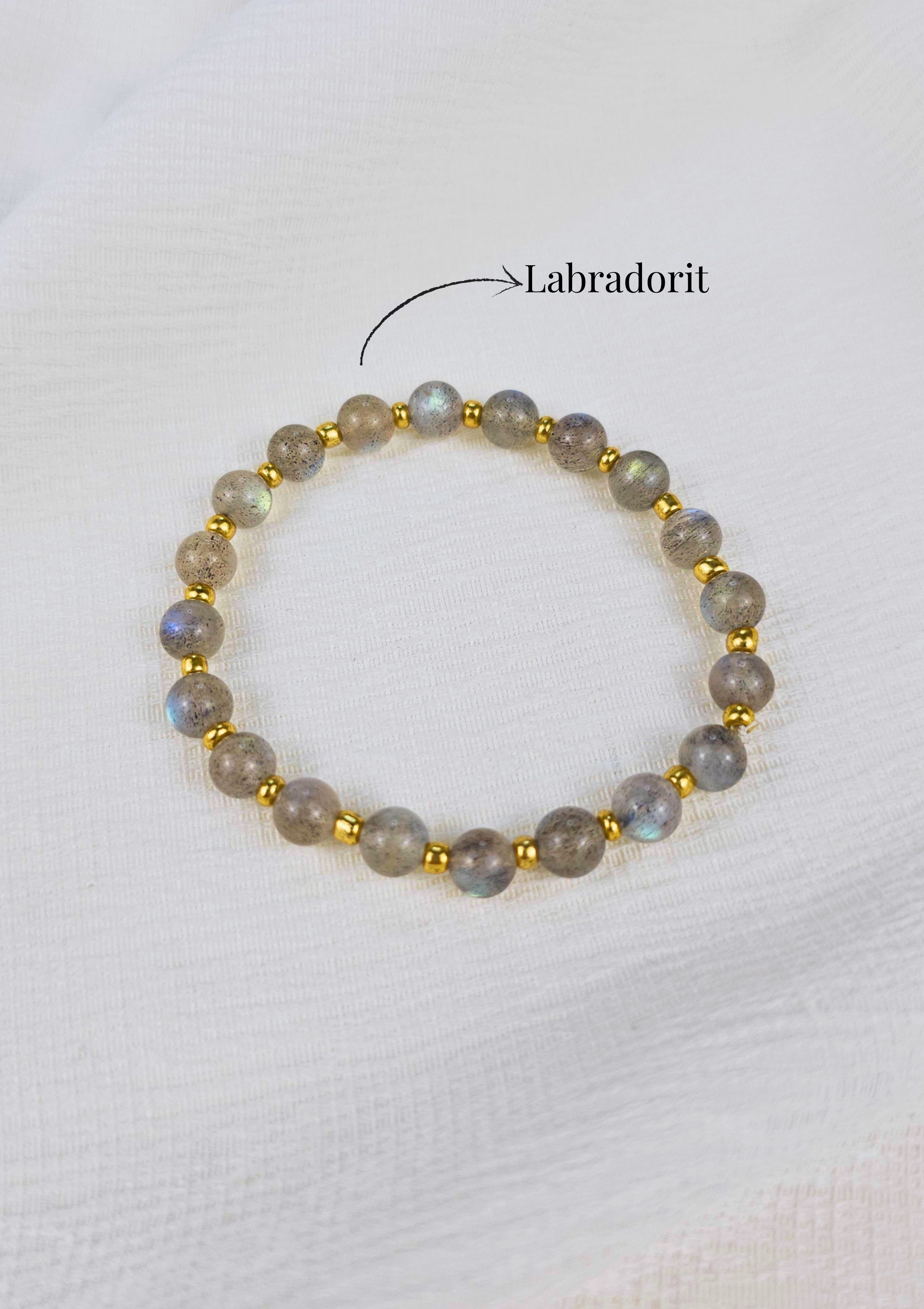Handgefertigtes Lunéa Edelsteinarmband aus echtem Labradorit mit goldfarbenen Details auf hellem Stoffhintergrund.