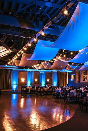 A reception room with Blue uplighting, tables and chairs and a dance floor